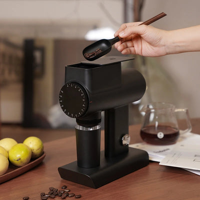 TIMEMORE Sculptor 064s grinder with a hand using a spoon to add coffee beans, showcasing its sleek design.