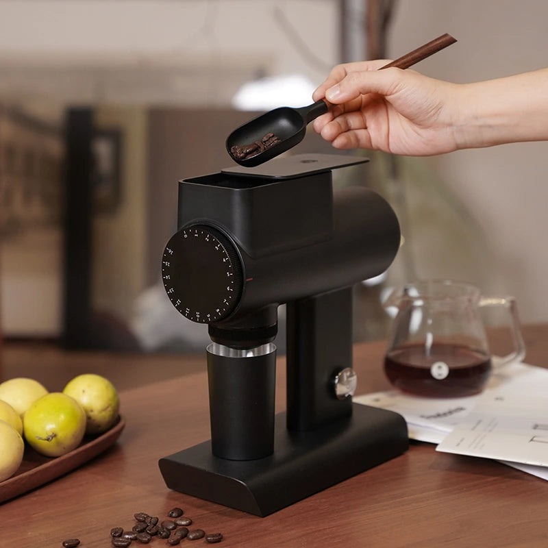 TIMEMORE Sculptor 064s grinder with a hand using a spoon to add coffee beans, showcasing its sleek design.