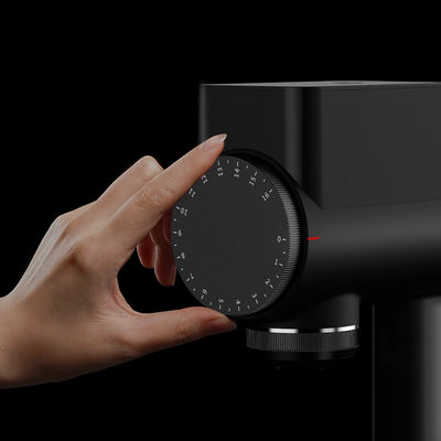 Hand adjusting the grind size dial on the TIMEMORE Sculptor 064s grinder for precise espresso preparation.